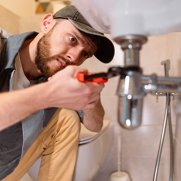 A plumber carefully fixes a leak in a sink using a wrench