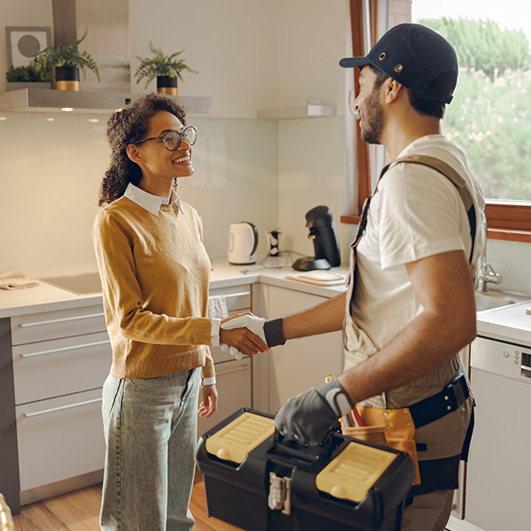 Male plumber shaking hands with happy female client while standing at home kitchen