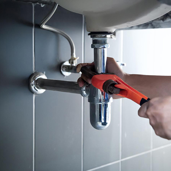Plumber using wrench to repair water pipe under sink